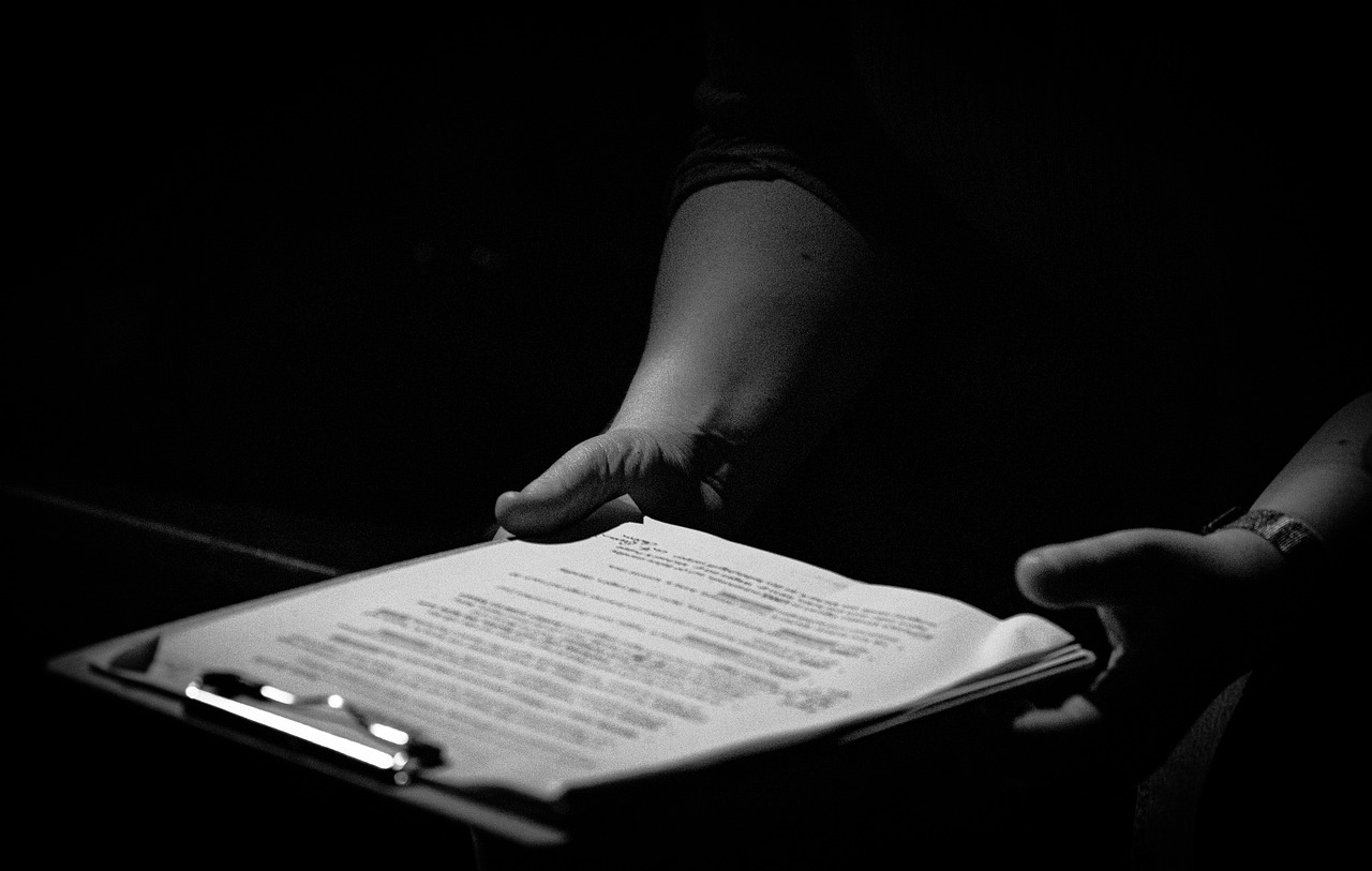 Greyscale image of hands holding a clipboard with paperwork on it