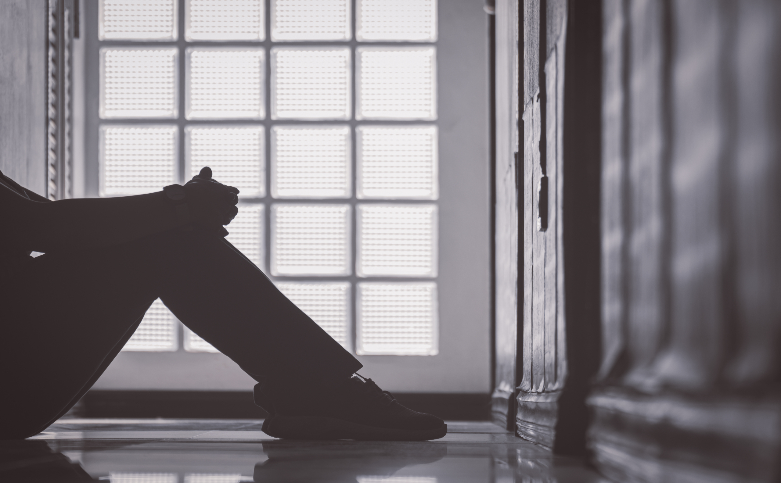 Low section of depressed woman sitting alone with hugging her knees on corridor at apartment in low key and monochrome style, mental health concept