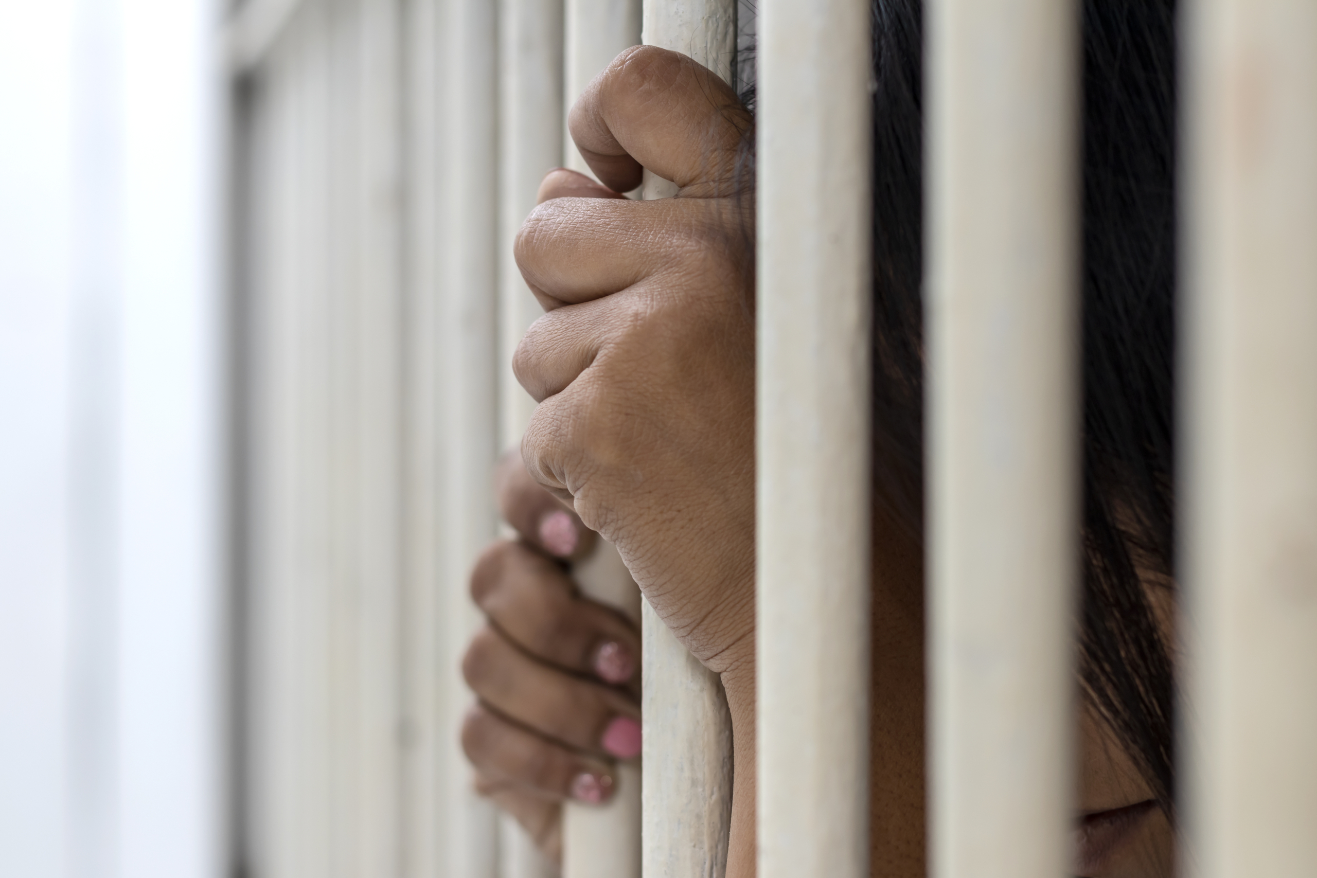 Close-up photos of the woman accused of fisting at the bars of the white iron cell and having a hidden face, a sad grief in the background blurred.