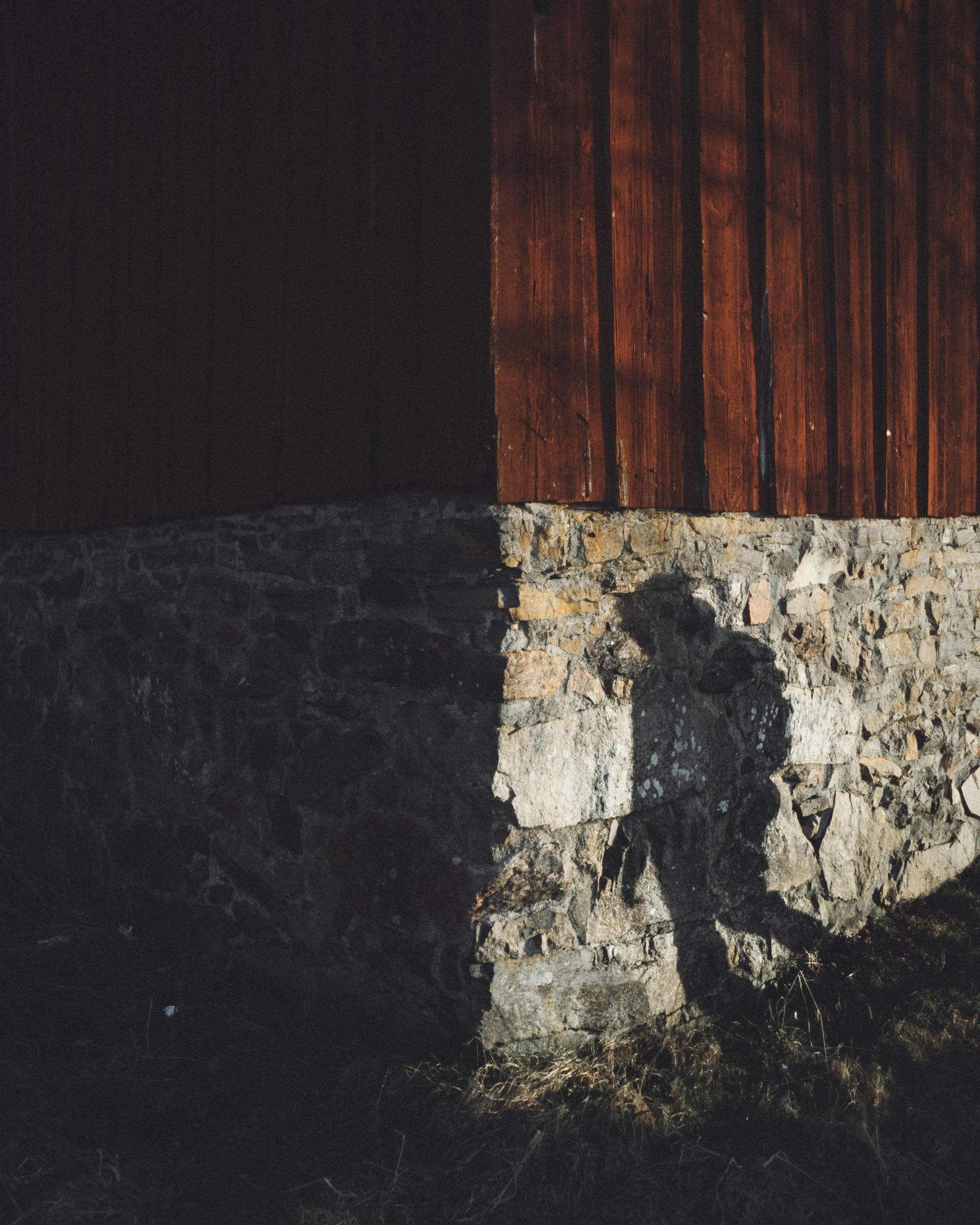 Shadow of a person against a stone building walking ominously towards darkness