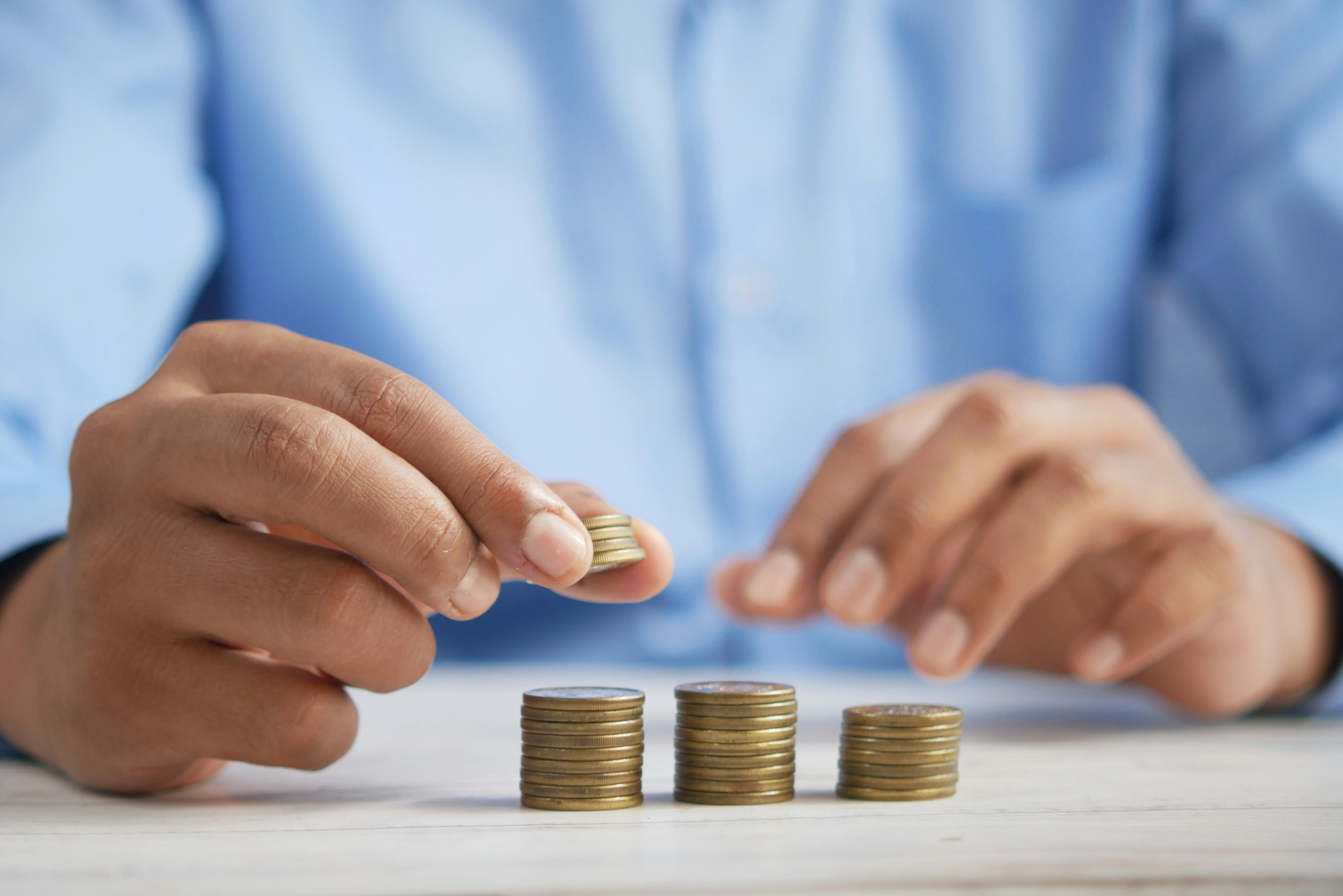 A person in a blue business shirt balances coins in three stacks