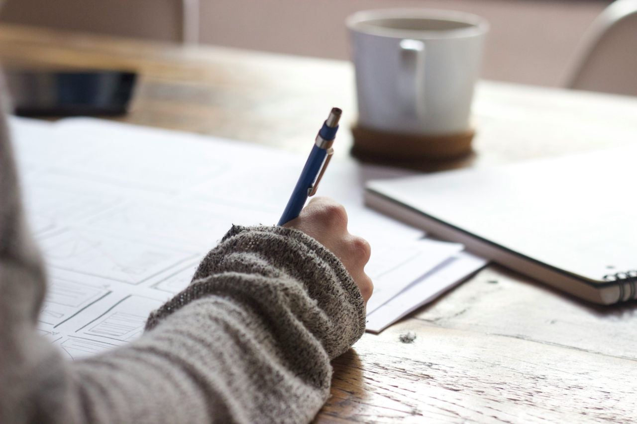 The forearm and hand of a person can be seen writing with a pen on some documents