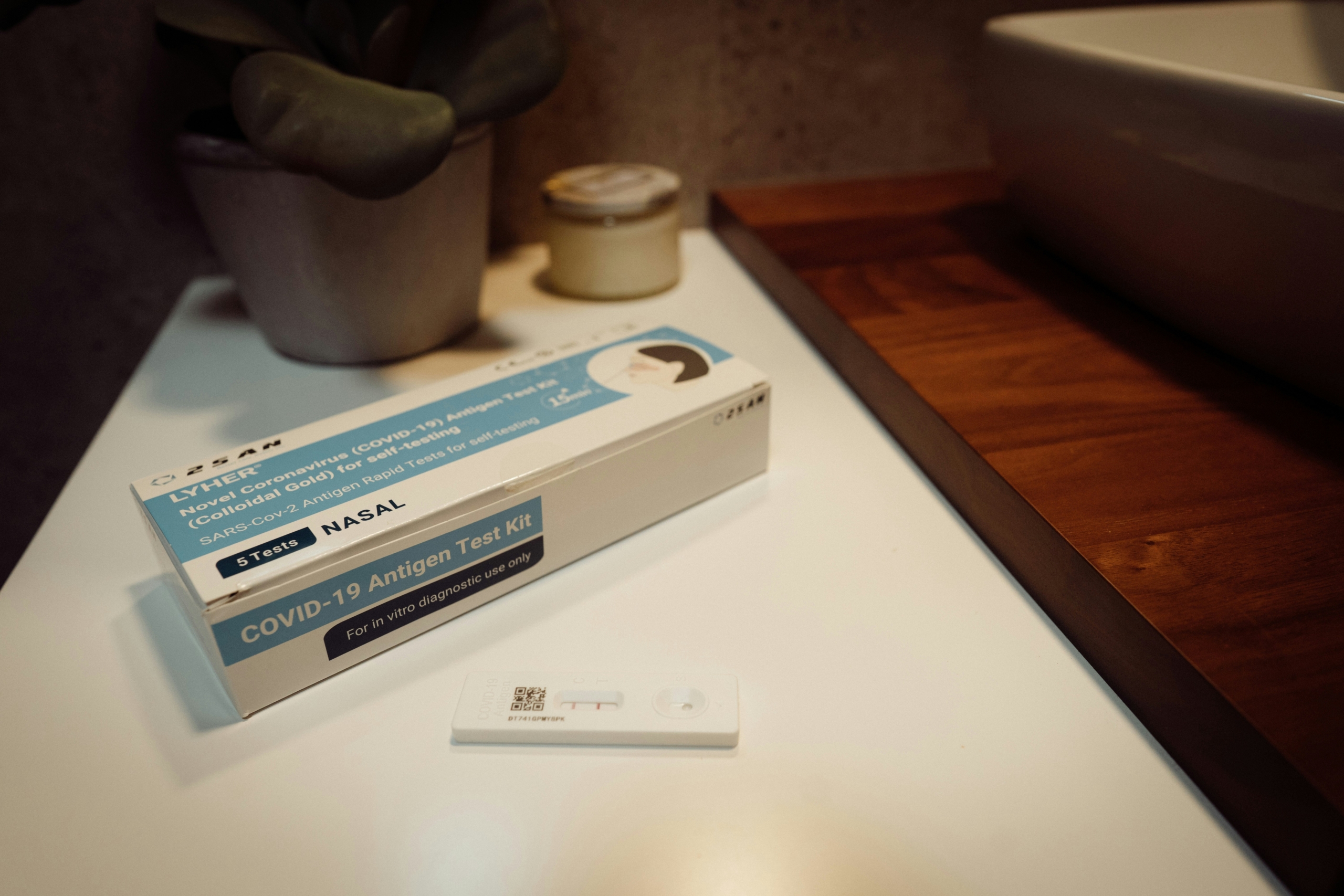 A COVID-19 Rapid Antigen Test Kit box sits on a counter, with the test itself nearby and displaying a positive result