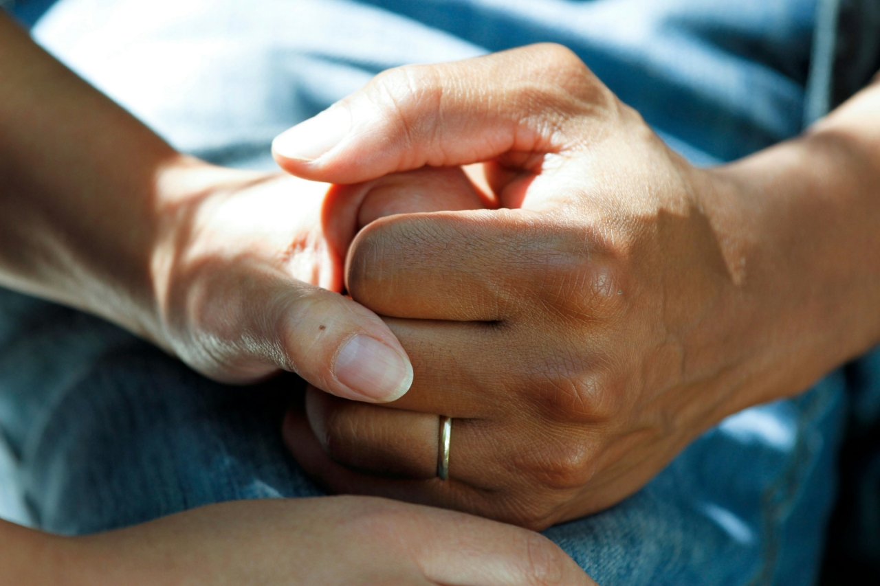 Two people clasp hands on top of a hospital sheet