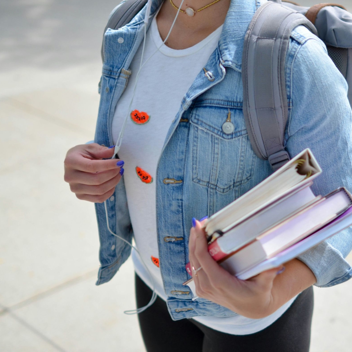 Woman in denim jacket with backpack holding books
