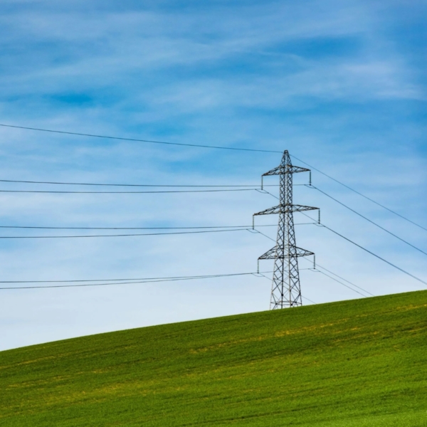 Power pylon on green hill with blue sky