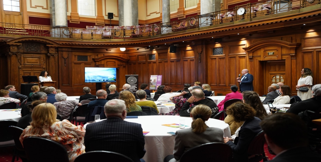 People sitting at tables at Parliament, looking at screen