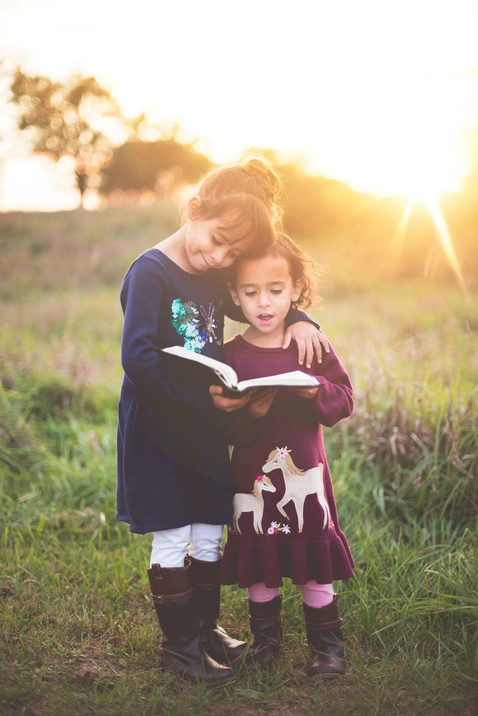 Two children standing in field reading book together