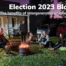 This postcard has an image of 7 people around a campfire at dusk. It is a joyful scene featuring at least three different generations. The words say: Election Blog 2023 - the benefits of intergenerational spaces.